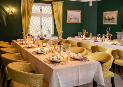 Weiss gedeckte Tafel mit grünen Stühlen im Speparee. Eingedeckt mit Tellern Gläsern und Servietten