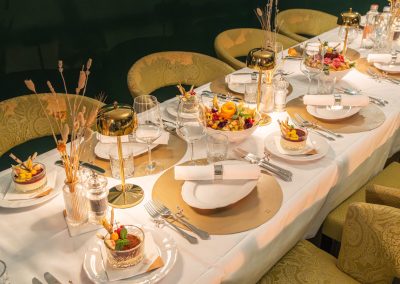 Weiss gedeckte Tafel mit grünen Stühlen im Speparee. Eingedeckt mit Tellern Gläsern und Servietten. Speisen in der Mitte des Tisches